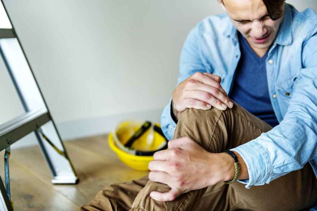 A contractor holds his injured knee after a fall