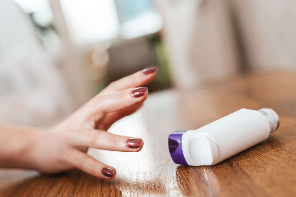 Asthma attack. A woman's hand is tensely reaching for an inhaler of medicine lying on the table. Indoor. Close up of hand