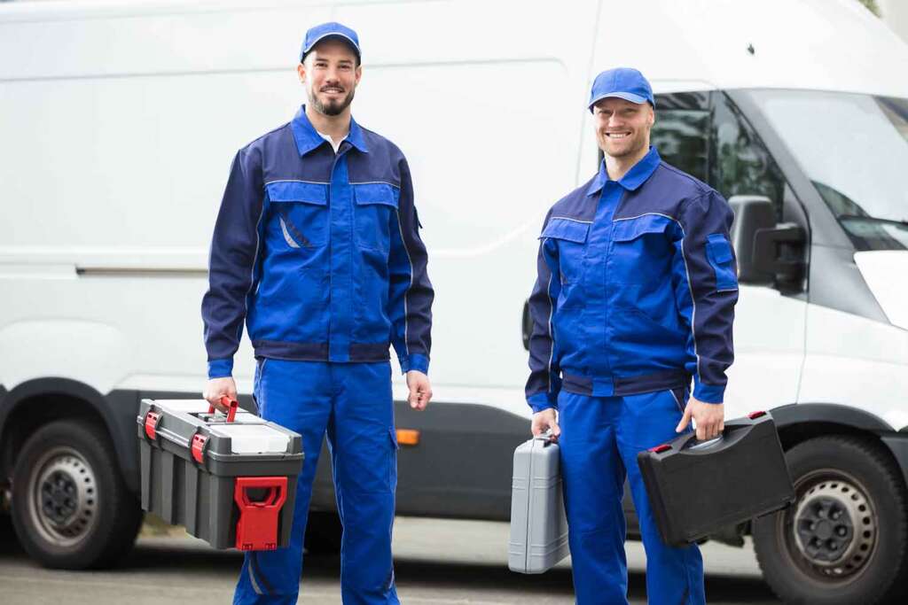 Two professional technicians in uniform stand in front of their van