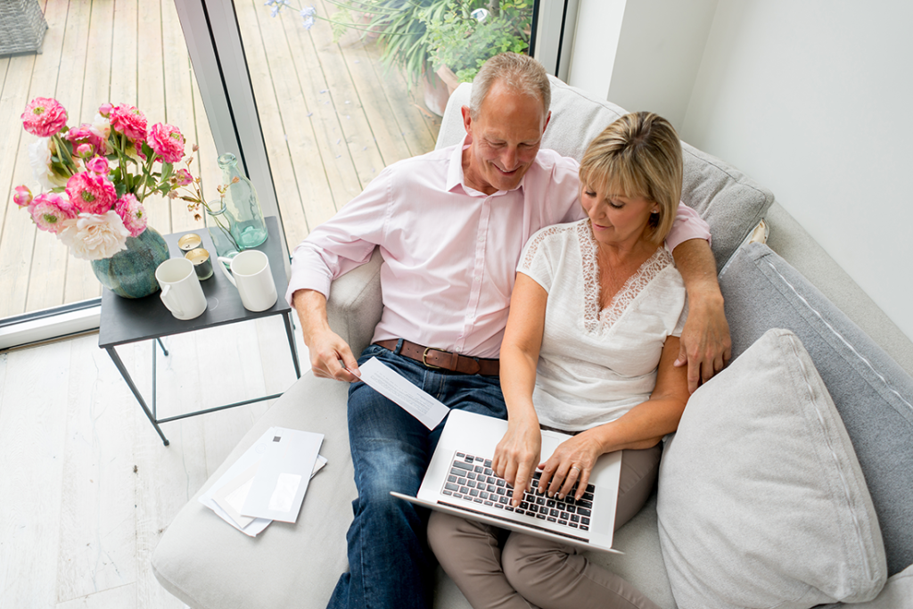 Man and woman share the sofa while paying bills on a laptop